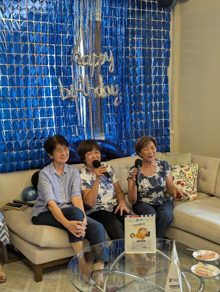 Olivan Sisters singing into microphones with joyful laughter on the couch